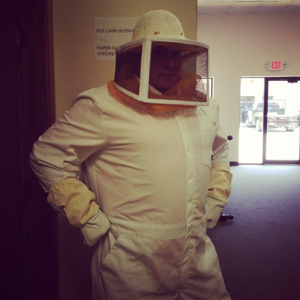 Pest control technician wearing a full white protective bee suit with a mesh veil, helmet, and heavy gloves.